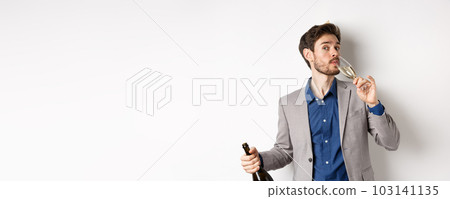Celebration and holidays concept. Handsome bearded man in suit and birthday hat holding bottle, drinking glass of champagne, standing on white background Celebration and holidays concept. Handsome bearded man in suit and birthday hat holding bottle, drinking glass of champagne, standing on white background 103141135