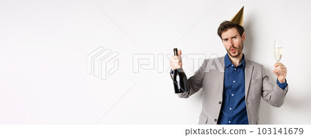 Celebration and holidays concept. Happy man in suit having fun at party, wearing birthday hat, dancing with champagne and drinking alcohol Celebration and holidays concept. Happy man in suit having fun at party, wearing birthday hat, dancing with champagne and drinking alcohol 103141679