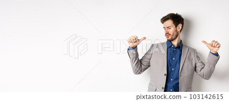 Handsome and confident man in suit pointing at himself, feeling cool and sassy, self-promoting his good appearance, standing on white background 103142615