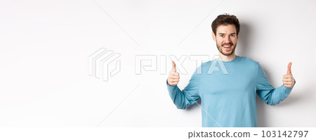 Cheerful young man showing thumbs up and smiling, recommend good product, praising choice, standing on white background 103142797