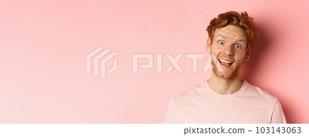 Headshot of funny redhead guy showing tongue, making silly faces at camera, standing joyful against pink background Headshot of funny redhead guy showing tongue, making silly faces at camera, standing joyful against pink background 103143063