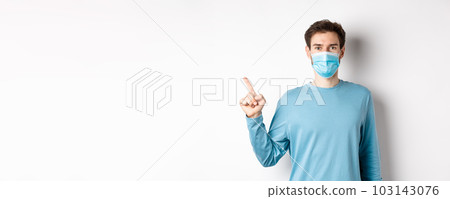 Coronavirus, health and quarantine concept. Caucasian man in medical mask pointing finger left, showing logo, standing in casual clothes on white background Coronavirus, health and quarantine concept. Caucasian man in medical mask pointing finger left, showing logo, standing in casual clothes on white background 103143076