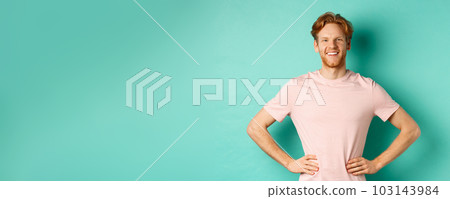 Enthusiastic young man with red hair, wearing t-shirt, standing happy and proud with hands on hops, standing over turquoise background Enthusiastic young man with red hair, wearing t-shirt, standing happy and proud with hands on hops, standing over turquoise background 103143984