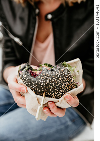 Close up of woman hands holding delicious organic salmon vegetarian burger on open air beer an burger urban street food festival in Ljubljana, Slovenia 103144041