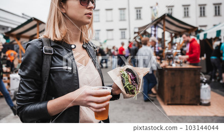 Close up of woman hands holding delicious organic salmon vegetarian burger and homebrewed IPA beer on open air beer an burger urban street food festival in Ljubljana, Slovenia 103144044