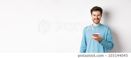 Celebration. Handsome young man celebrating birthday, holding bday cake with lit candle and smiling, making wish, standing over white background 103144045