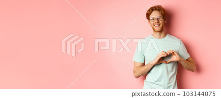 Valentines day concept. Handsome redhead man in glasses, showing heart sign and say I love you, standing over pink background 103144075