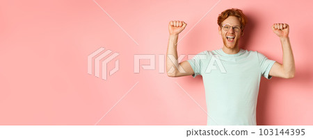 Happy winner with red hair and beard celebrating victory, shouting yes with joy and raising hands up, enjoy success, standing over pink background Happy winner with red hair and beard celebrating victory, shouting yes with joy and raising hands up, enjoy success, standing over pink background 103144395