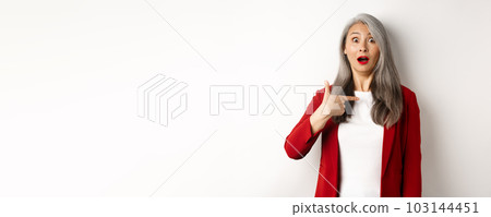 Surprised asian woman with grey hair, pointing at herself and gasping confused, standing over white background 103144451