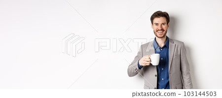 Handsome businessman in suit drinking coffee or tea from office mug, smiling enthusiastic at camera, standing against white background 103144503