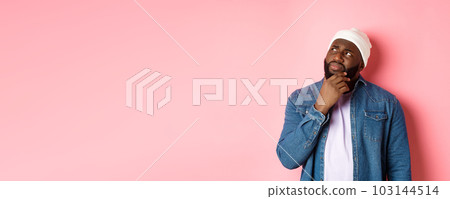 Image of puzzled and concerned black man, staring at upper left corner and thinking, making decision with doubts, standing over pink background 103144514