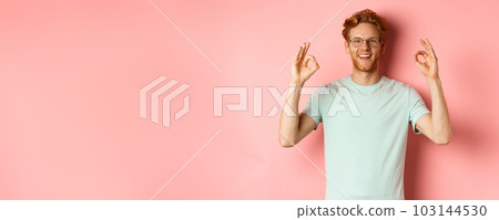 Satisfied caucasian man with red hair, wearing glasses and t-shirt, showing okay gestures and smiling, saying yes and approving something, standing over pink background Satisfied caucasian man with red hair, wearing glasses and t-shirt, showing okay gestures and smiling, saying yes and approving something, standing over pink background 103144530