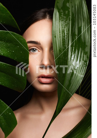 Beauty Portrait of brunette girl in palm leaves. Beautiful young woman with Make-up 103145083