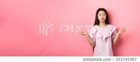 Stay calm. Peaceful asian woman meditating, hold hans in zen gseture and close eyes, practice yoga, standing patient on pink background 103145367