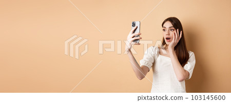 Fashion girl record smartphone blog, taking selfie on cellphone, standing on beige background Fashion girl record smartphone blog, taking selfie on cellphone, standing on beige background 103145600