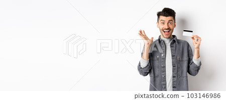 Excited man scream from joy and showing plastic credit card, rejoicing on shopping, standing against white background 103146986
