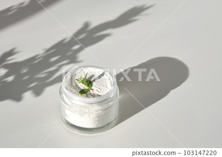 An open jar of facial scrub powder with a green sprig. 103147220