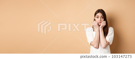 Cute and silly girl lean face on hands and looking dreamy at camera, standing romantic on beige background Cute and silly girl lean face on hands and looking dreamy at camera, standing romantic on beige background 103147273