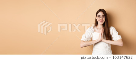 Smiling girl in glasses say thank you, show namaste gesture, express gratitude, standing pleased on beige background 103147622