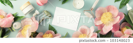 Top view of natural cosmetics and pink peonies on pastel blue background with white card for invitation, logo or design 103148023