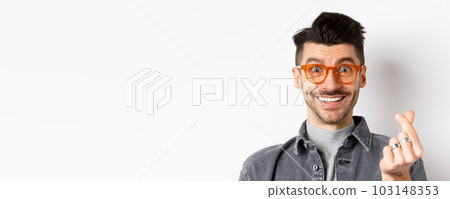 Close up portrait of cute guy with moustache wearing glasses, showing hand heart sign, smiling happy, standing on white background 103148353
