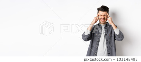 Man with headache grimacing and clenching teeth from painful migraine, touching head temples, suffering migraine, need painkillers, standing on white background 103148495