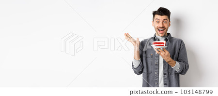 Excited man celebrating birthday, looking happy, holding cake with candle, making wish, standing happy against white background 103148799