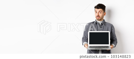 Indecisive young man pouting and shrugging while showing empty laptop screen, standing clueless on white background 103148823