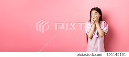 Shocked and startled asian woman looking aside at logo, covering mouth with hands speechless, standing in dress on pink background Shocked and startled asian woman looking aside at logo, covering mouth with hands speechless, standing in dress on pink background 103149161