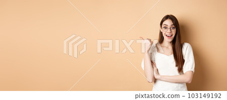 Excited girl in glasses pointing aside at logo, smiling amazed, recommending company, standing on beige background Excited girl in glasses pointing aside at logo, smiling amazed, recommending company, standing on beige background 103149192