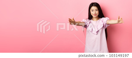 Cute teen asian girl stretch out hands for hug, want to cuddle, friendly greeting you, standing on pink background 103149197