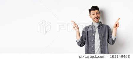 Cheerful smiling man pointing fingers sideways, showing left and right ways, looking happy at camera, standing on white background 103149458