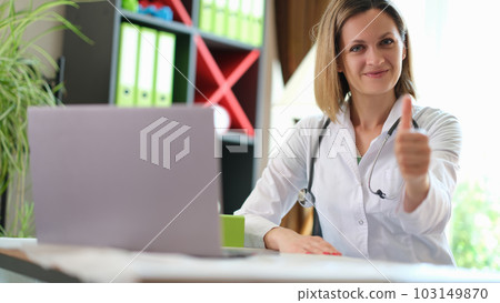 Satisfied doctor shows thumb up gesture sitting at table Satisfied doctor shows thumb up gesture sitting at table 103149870