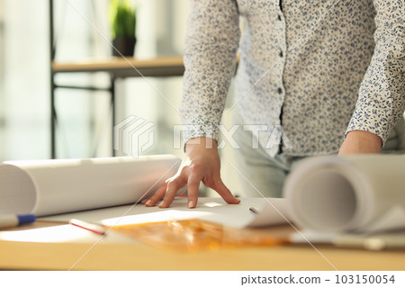 Female engineer unrolls large paper with building drawing Female engineer unrolls large paper with building drawing 103150054