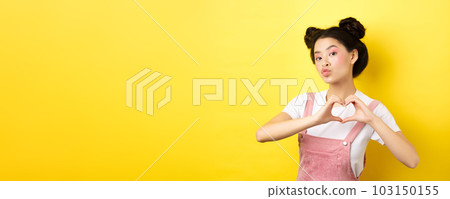 Silly japanese girl showing heart gesture and wishing happy Valentines day, pucker lips to kiss lover, standing on yellow background Silly japanese girl showing heart gesture and wishing happy Valentines day, pucker lips to kiss lover, standing on yellow background 103150155