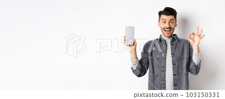Excited smiling guy showing empty smartphone screen with okay gesture, recommending app or shopping offer, standing on white background Excited smiling guy showing empty smartphone screen with okay gesture, recommending app or shopping offer, standing on white background 103150331