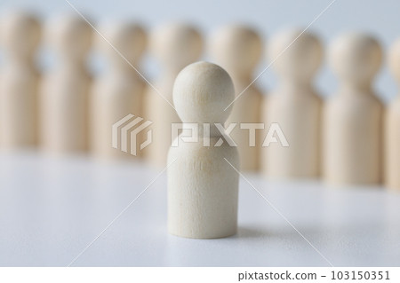 White wooden figure stands against blurred figurines in row White wooden figure stands against blurred figurines in row 103150351