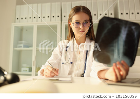 Concentrated doctor in glasses examines X-ray of patient Concentrated doctor in glasses examines X-ray of patient 103150359