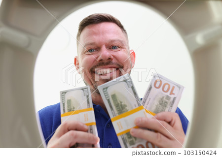 Smiling man looks into toilet bowl holding wads of dollars Smiling man looks into toilet bowl holding wads of dollars 103150424