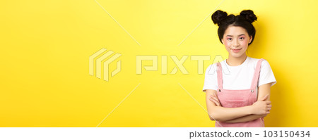 Beauty asian girl with glamour makeup, cross arms on chest and smiling tenderly at camera, standing on yellow background 103150434