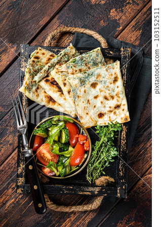 Baked Gozleme flatbread with greens in a box with vegetable salad. Wooden background. Top view 103152511