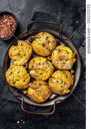 Broken potatoes baked in oil with herbs. Black background. Top view Broken potatoes baked in oil with herbs. Black background. Top view 103152535