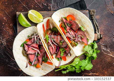Carne Asada Tacos with grilled steak, green sauce, jalapenos and onion, Mexican food. Dark background. top view Carne Asada Tacos with grilled steak, green sauce, jalapenos and onion, Mexican food. Dark background. top view 103152537