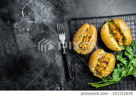 Turkish Kumpir, baked potatoes stuffed with cheese, bacon, salty cucumber, herbs and butter. Black background. Top view. Copy space 103152638