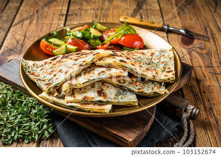 Gozleme flatbread with greens and vegetable salad on garnish. Wooden background. Top view Gozleme flatbread with greens and vegetable salad on garnish. Wooden background. Top view 103152674