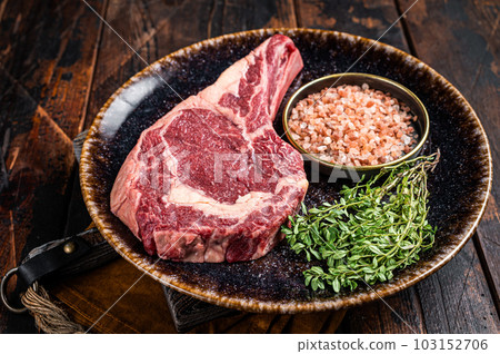 Raw prime cowboy or rib eye steak, dry aged beef meat. Wooden background. Top view Raw prime cowboy or rib eye steak, dry aged beef meat. Wooden background. Top view 103152706