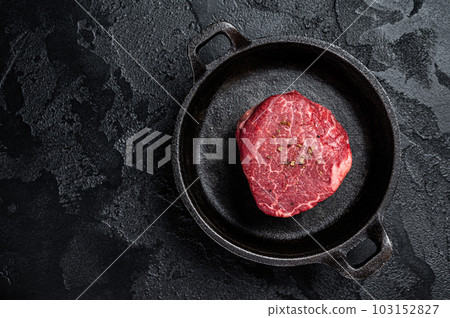 Fillet Mignon prime beef steak, raw dry aged marble meat with herbs and spices ready for cooking. Black background. Top view. Space for text 103152827