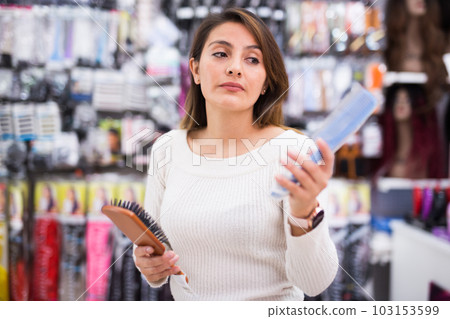 Interested young woman selecting comb for hair in shop Interested young woman selecting comb for hair in shop 103153599