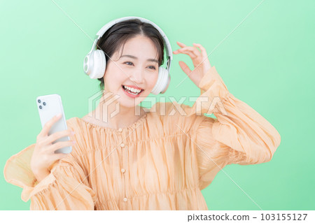 Young woman listening to music on smartphone with headphones on green background Young woman listening to music on smartphone with headphones on green background 103155127