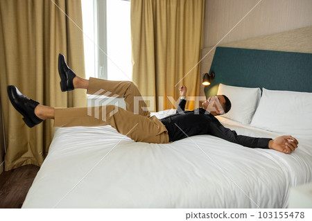 Young man lying on bed in the hotel rooma and feeling relaxed 103155478